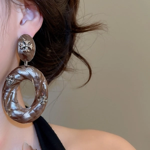 Detailed close-up of acrylic hoop earring featuring marble texture and metallic cross icons