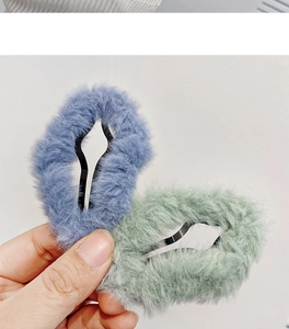 Close-up of hand holding plush blue and green hair clips with fuzzy texture and metal grip