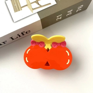 Cute orange-shaped hair claw clip with pink bows and yellow leaves on a book background
