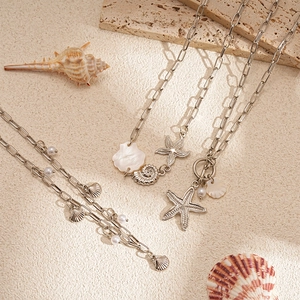 Close-up of ocean-themed necklace set with starfish shells and faux pearls on sand