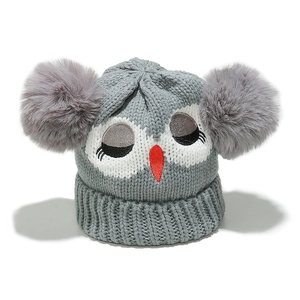 Detail of grey knitted kids hat featuring owl embroidery and two large faux fur pom-poms