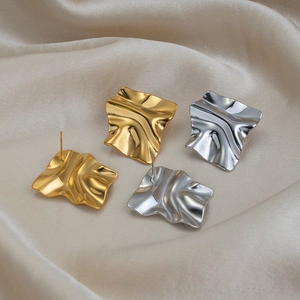 Irregular textured gold and silver square stud earrings on elegant beige silk fabric