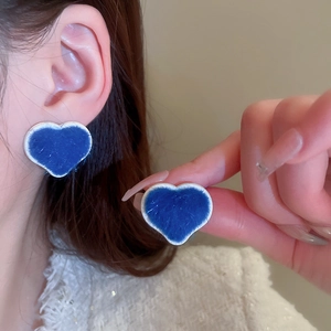 Close-up of blue flocked heart earrings with silver trim shown on ear and hand