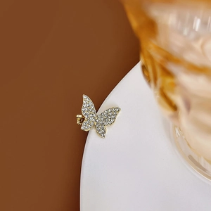 Détail macro d'un earcuff papillon doré avec oxydes de zirconium sur une assiette blanche