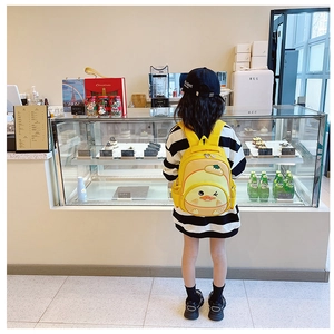 Rear view of a yellow cartoon duck backpack worn by a child in a cafe setting