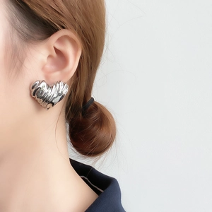 Close-up of heart-shaped silver earrings with pleated texture worn on a model's ear