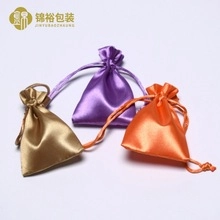 Detail of satin gift pouches with drawstring closures in gold, purple, and orange silk fabric