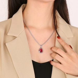 Detail of red teardrop diamond pendant on silver twist chain worn with a beige blazer