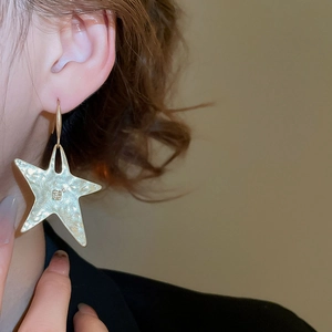 Close-up of gold star earrings with hammered metal texture worn by a model