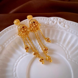 Macro detail of French vintage golden tassel earrings with ethnic Jhumka hollow pattern