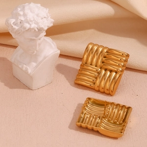 Close-up of golden square stud earrings with woven texture on silk fabric background