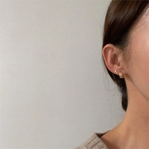 Détail d'un clou d'oreille croix dorée et créole texturée portés par le modèle