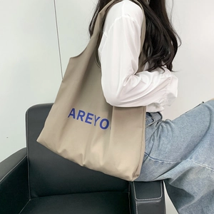 Close-up of a khaki canvas tote bag featuring blue letter print shown on a model