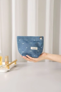 Detail of blue denim cosmetic bag with white bow pattern and golden floral zipper slider