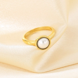Makroaufnahme eines vergoldeten Rings mit weißer Perle auf Seidenhintergrund