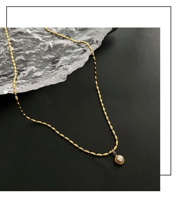 Detailed shot of golden rice bead chain with a round pearl pendant on black background
