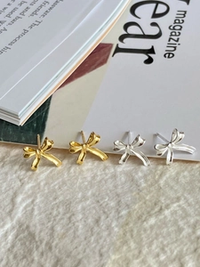 Close-up of elegant gold and silver ribbon bow stud earrings on a textured background