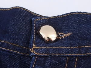 Makroaufnahme eines goldfarbenen Metallknopfes auf dunkelblauem Denim-Taillengewebe