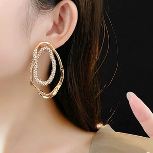 Macro close-up of large gold-plated oval stud earrings with sparkling crystals on model
