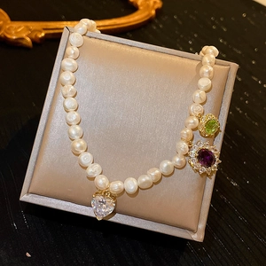 Detailed view of baroque pearl necklace featuring heart and colorful gemstone pendants