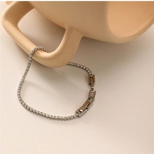 Détail d'un bracelet en chaîne argentée avec zircons posé sur une tasse en céramique