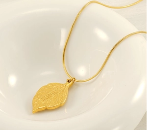 Detailed view of a gold leaf pendant with 'Yiye Shengcai' engraving in a ceramic bowl