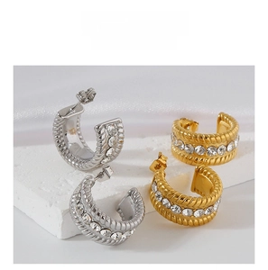 Close-up of gold and silver C-shaped twist earrings with inlaid cubic zirconia crystals