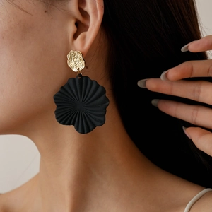 Close-up of matte black floral drop earrings with hammered gold metal disc on model