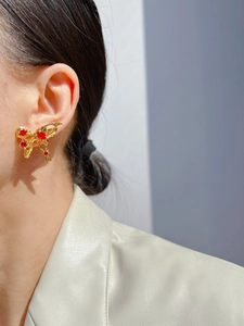 Close-up of golden liquid metal butterfly earring with red zircon on a model's ear