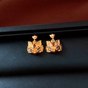 Macro shot of gold fox earrings with red gemstones and sparkling zircon details