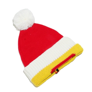 Vue détaillée d'un bonnet de Noël tricoté rouge et jaune avec un pompon blanc doux.