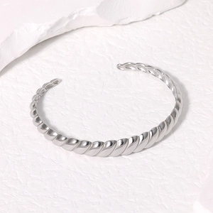 Detail shot of silver twisted titanium steel open bangle on white stone surface