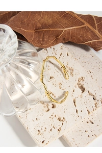 Close-up of golden braided knot open bangle on natural stone base with elegant finish