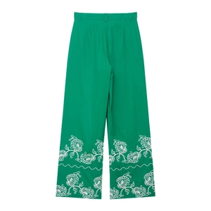 Détail de broderie florale blanche sur l'ourlet d'un pantalon large en lin vert
