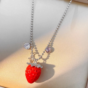 Dettaglio della collana con fragola rossa e ciondoli in cristallo su tessuto beige