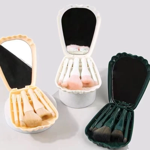 Three makeup brush sets in shell-shaped mirror cases in beige, white, and dark green