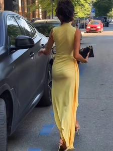 Detail of a bright yellow sleeveless maxi dress featuring a high collar and pleated slit hem