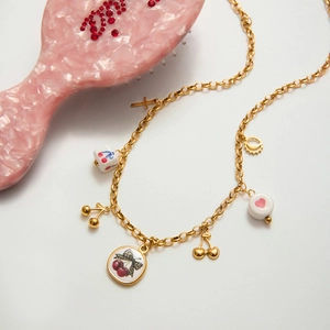 Détail de la chaîne en acier doré 18K avec pendentifs cerise et breloques vintage