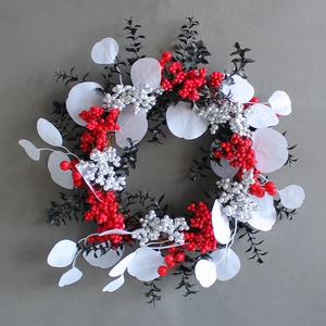 Weihnachtskranz mit roten Beeren und weißen Blättern auf grauem Hintergrund
