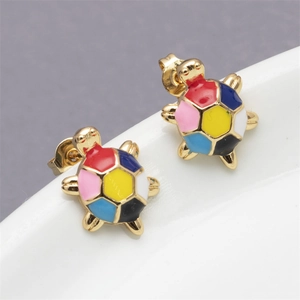 Close-up of golden turtle stud earrings with colorful enamel inlay on white tray