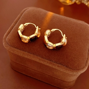 Close-up of golden huggie hoop earrings with amber stones on brown velvet display