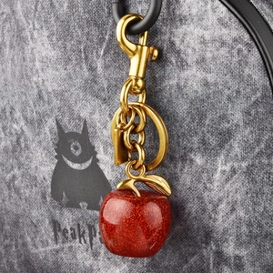 Golden metal keychain with a red glitter apple pendant attached to a grey textured bag