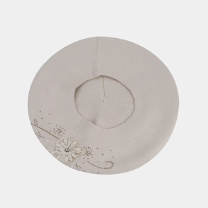 Dettaglio di un basco in maglia beige con applicazione floreale e perline dorate