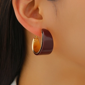 Close-up of elegant C-shaped gold-plated hoop earrings with deep red enamel finish