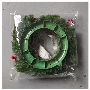 Detail of a Christmas wreath with red berries and pine needles in clear plastic packaging