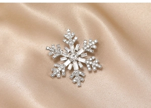 Macro shot of silver snowflake brooch with white cubic zirconia on champagne silk fabric