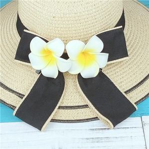 Détail d'un chapeau de paille avec ruban noir et fleurs de frangipanier sur bois bleu
