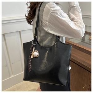 Schwarze Leder-Tragetasche mit Baseball-Anhänger am Model in minimalistischem Raum