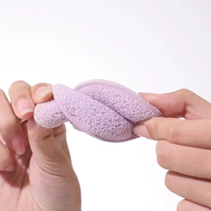 Flexible purple cleansing sponge being twisted to demonstrate its soft and elastic texture