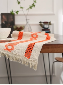 Macro detail of bohemian hollowed-out woven table runner with orange tassels on dark wood